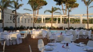 An outdoor dining area with tables set for a meal, surrounded by palm trees and a pool. - Agriturismo Campo Allegro (Santa Ninfa)