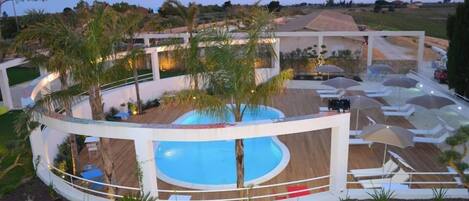 A modern poolside area with a circular pool, lounge chairs, umbrellas, and a wooden deck.