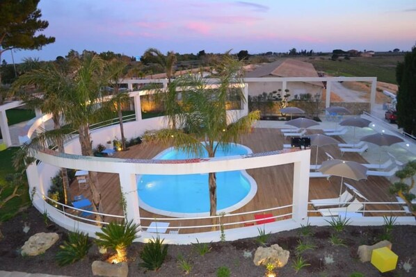 A modern poolside area with a circular pool, lounge chairs, umbrellas, and a wooden deck. - Agriturismo Campo Allegro (Santa Ninfa)