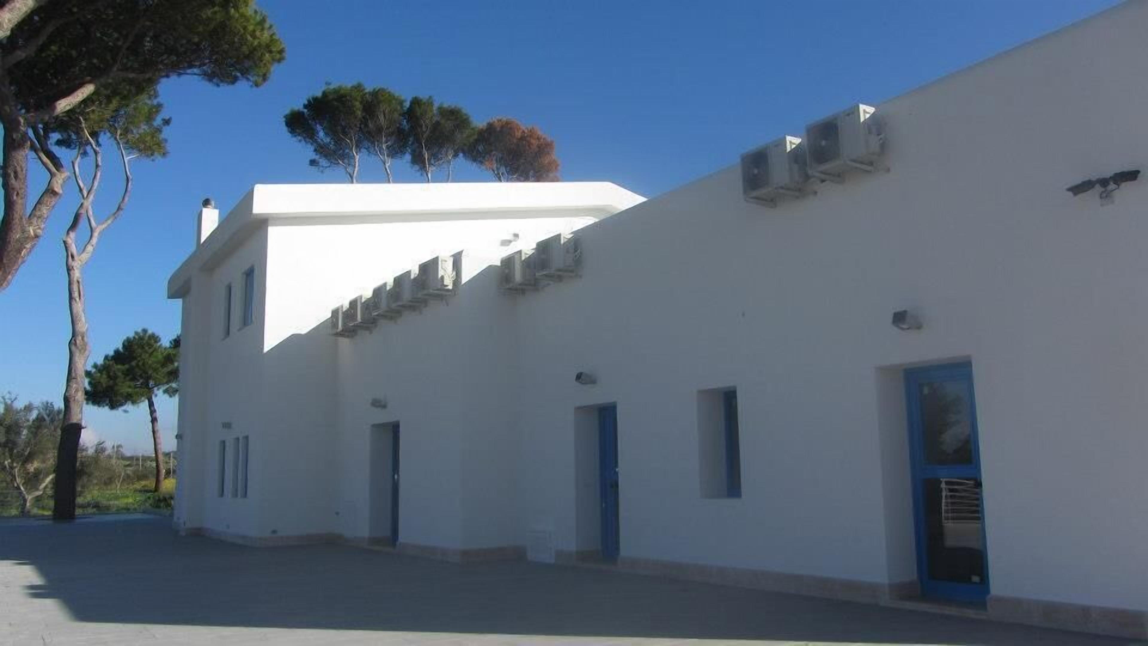 A white building with multiple doors and windows, air conditioning units, and a clear sky.