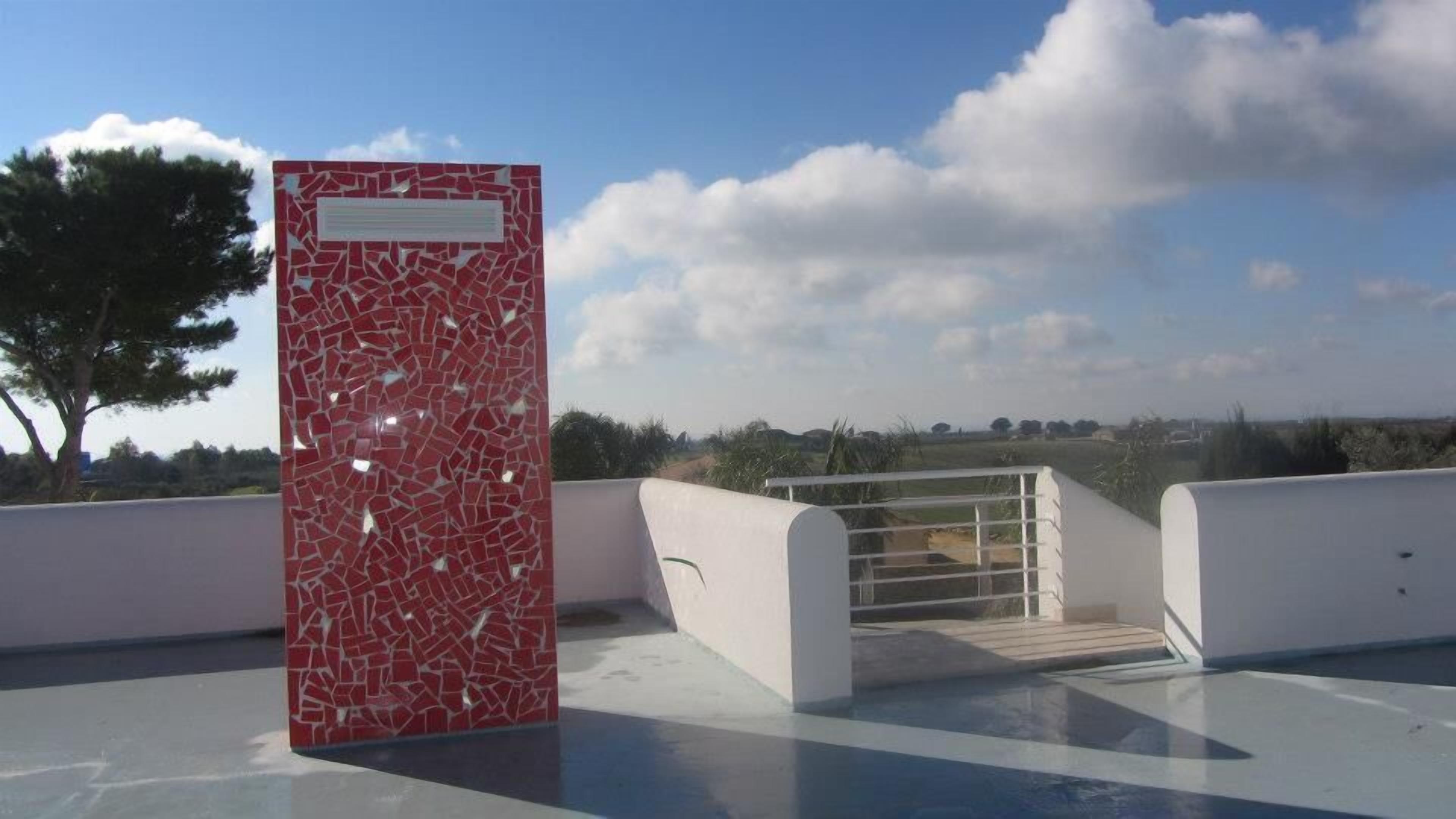 A rooftop pool area with a red mosaic wall and a clear view of the surrounding landscape.