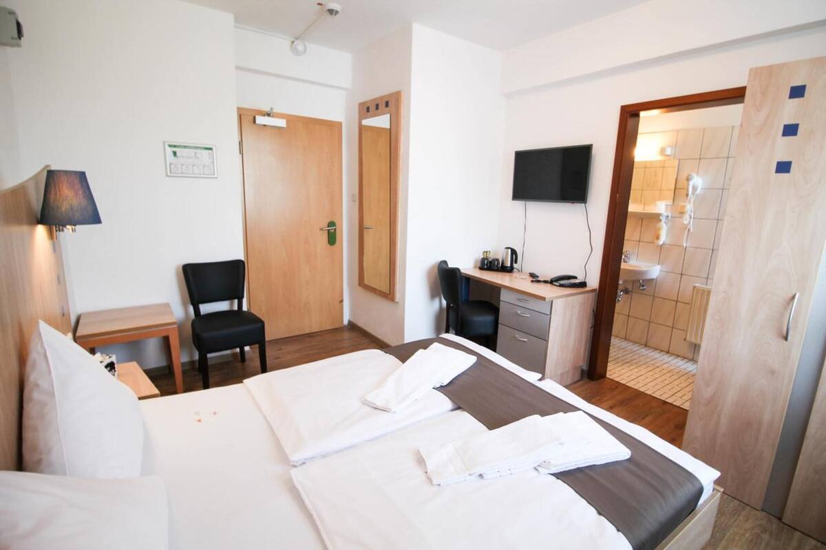 A hotel room with a bed, desk, chair, TV, and a bathroom visible through an open door.