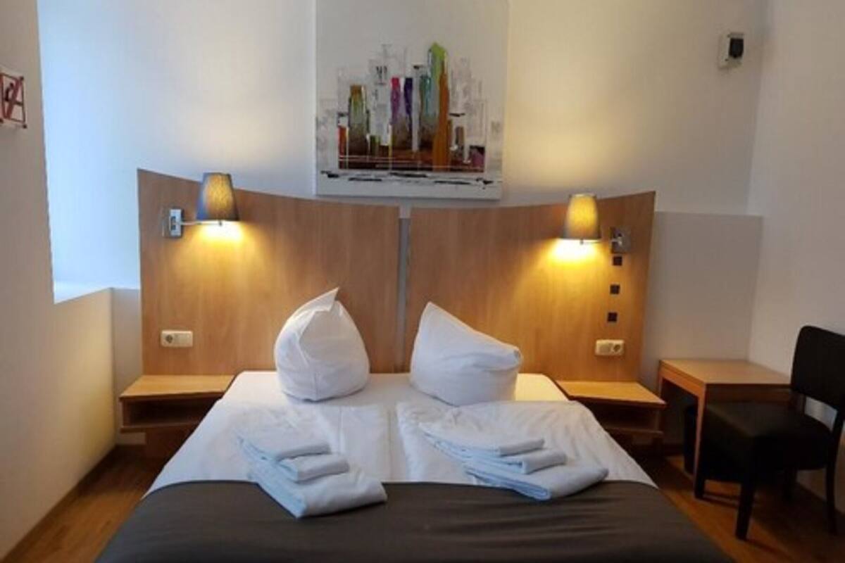 A hotel room with a bed, two bedside tables, a chair, and a wall-mounted artwork above the bed.