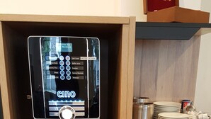 A coffee machine with a digital menu, white mugs, and glassware on shelves. - Center Hotel Essen (Essen)