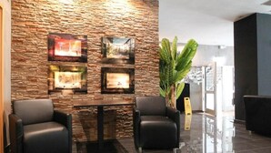 A lobby with a stone wall, framed pictures, a fireplace, two leather chairs, and a large plant. - Center Hotel Essen (Essen)
