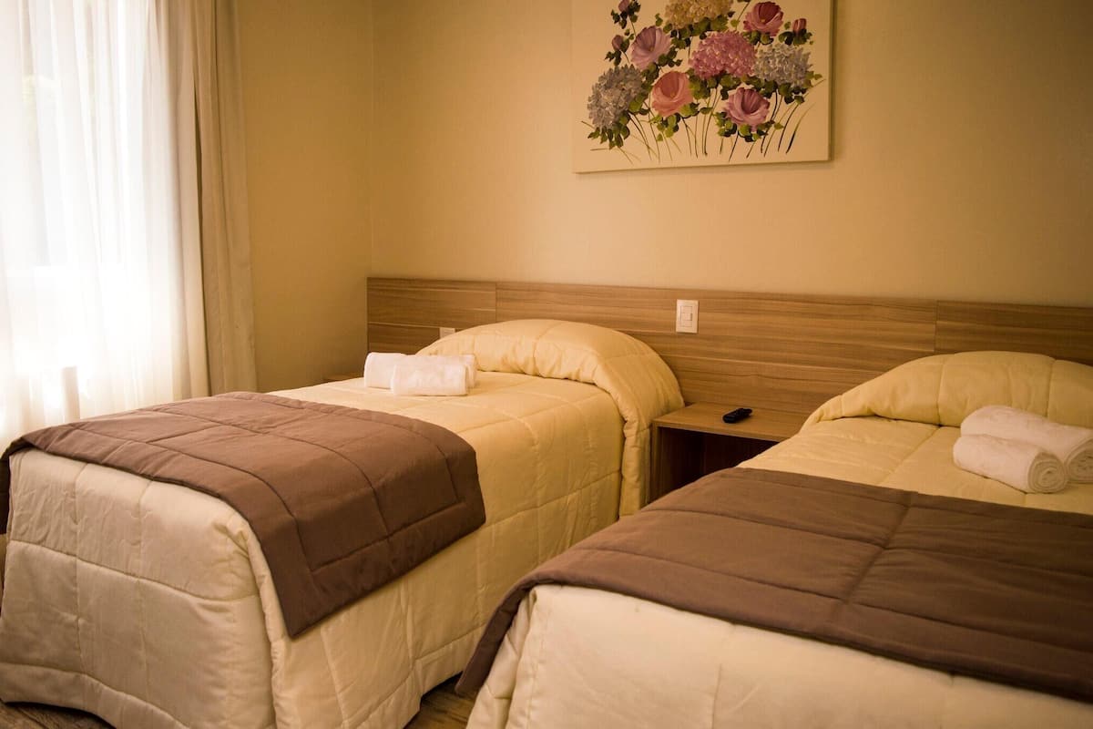 A hotel room with two beds, beige walls, and a floral painting above the beds.