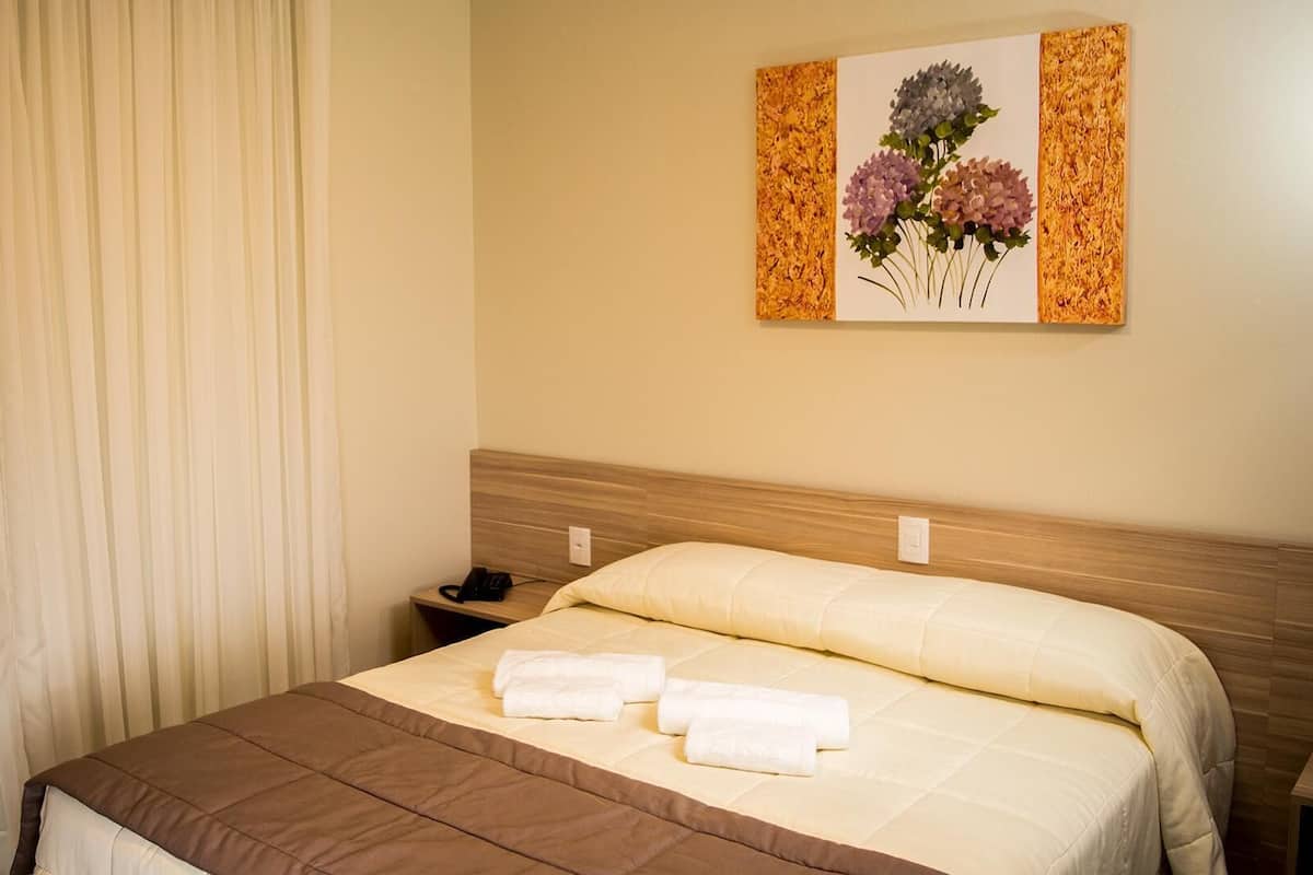A hotel room with a bed, a nightstand, a telephone, and a painting on the wall.
