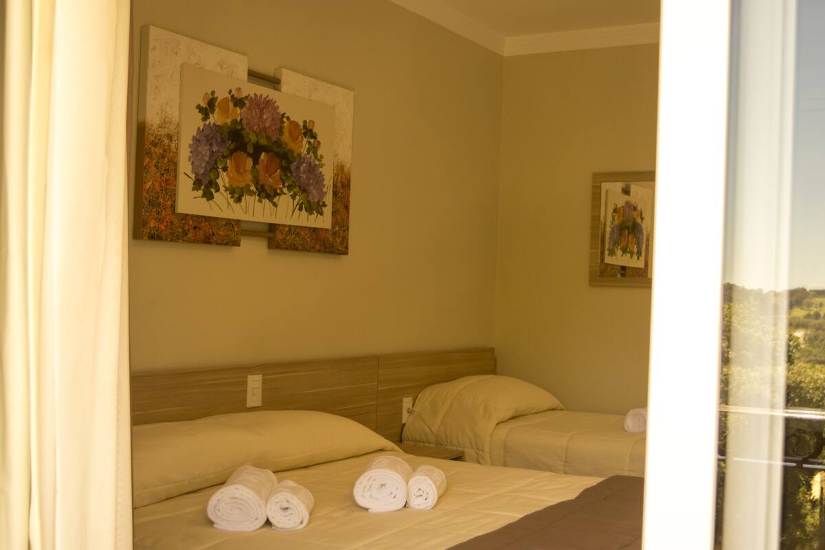 A hotel room with two beds, a painting of flowers on the wall, and a window with a view.