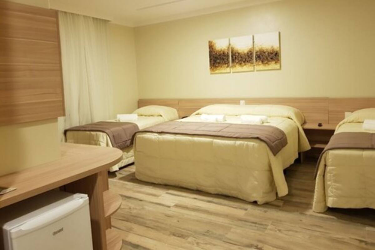 A hotel room with two beds, a small desk, and a refrigerator.