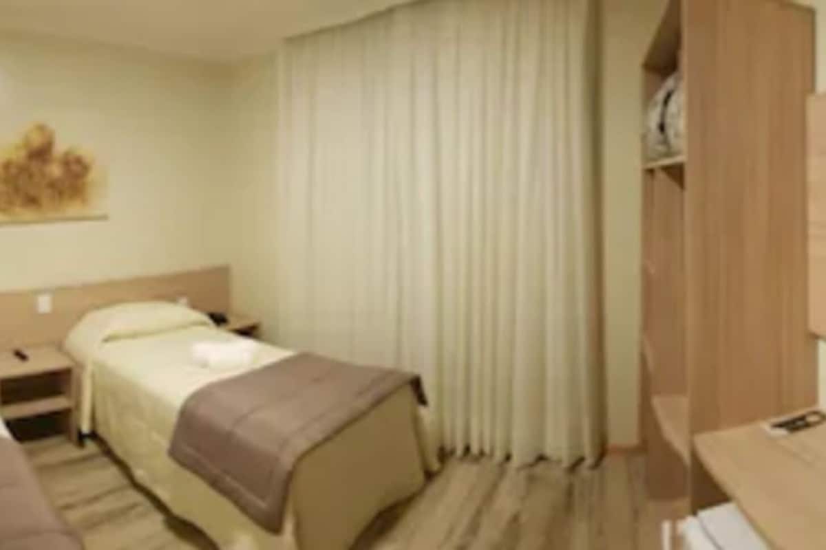 A hotel room with two beds, a desk, a TV, and a window with curtains.