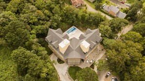 An aerial view of a large, multi-story house with a prominent swimming pool, surrounded by dense greenery. - Sky Serra Hotel (Gramado)