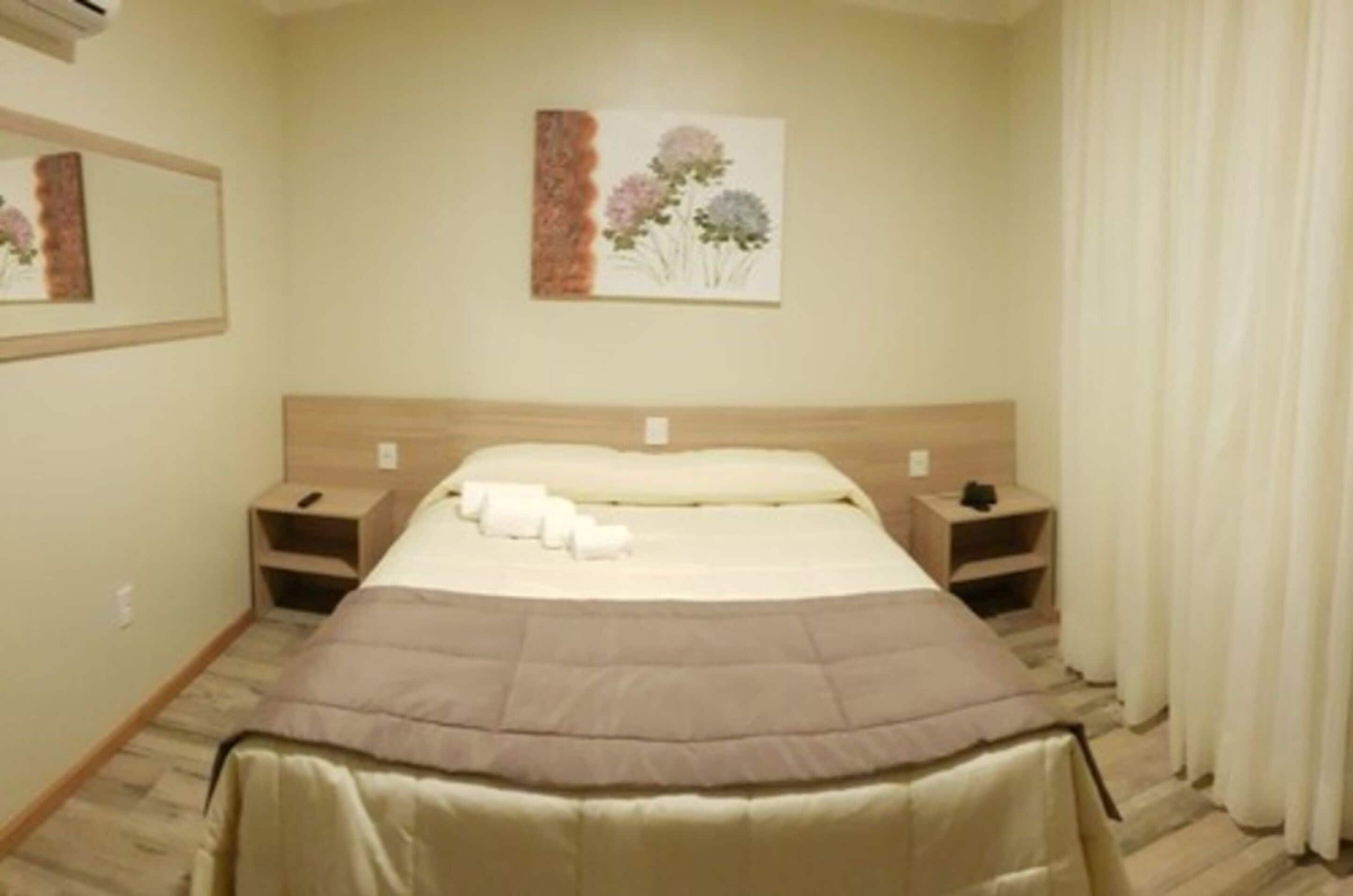 Un dormitorio ordenado con cama, mesitas de noche y una obra de arte colgada en la pared.