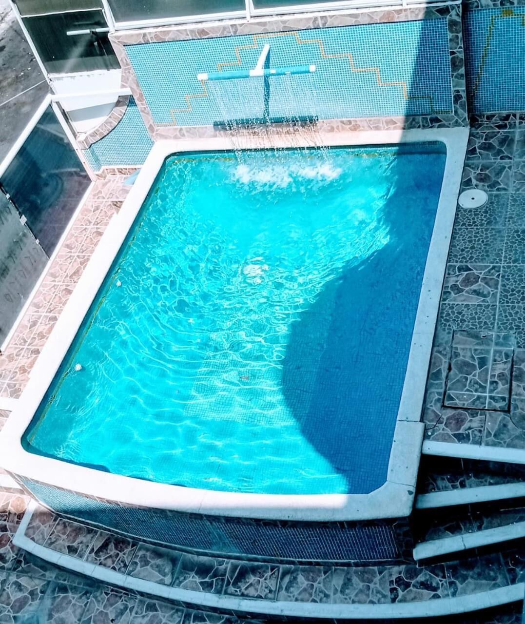 A rectangular swimming pool with a stone tile border and a mesh safety net.