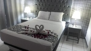 Una habitación de hotel con una cama grande, dos mesitas de noche con lámparas y un cabecero capitonado.