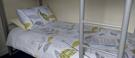 A bunk bed with a white and yellow leaf-patterned bedspread, a pillow with a similar design, and a metal ladder.