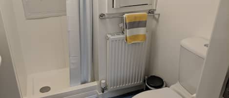 Un baño con ducha, inodoro y radiador.