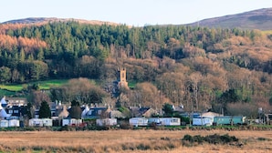 Een landelijk dorp met traditionele huizen, een kerk en een heuvel begroeid met bomen.