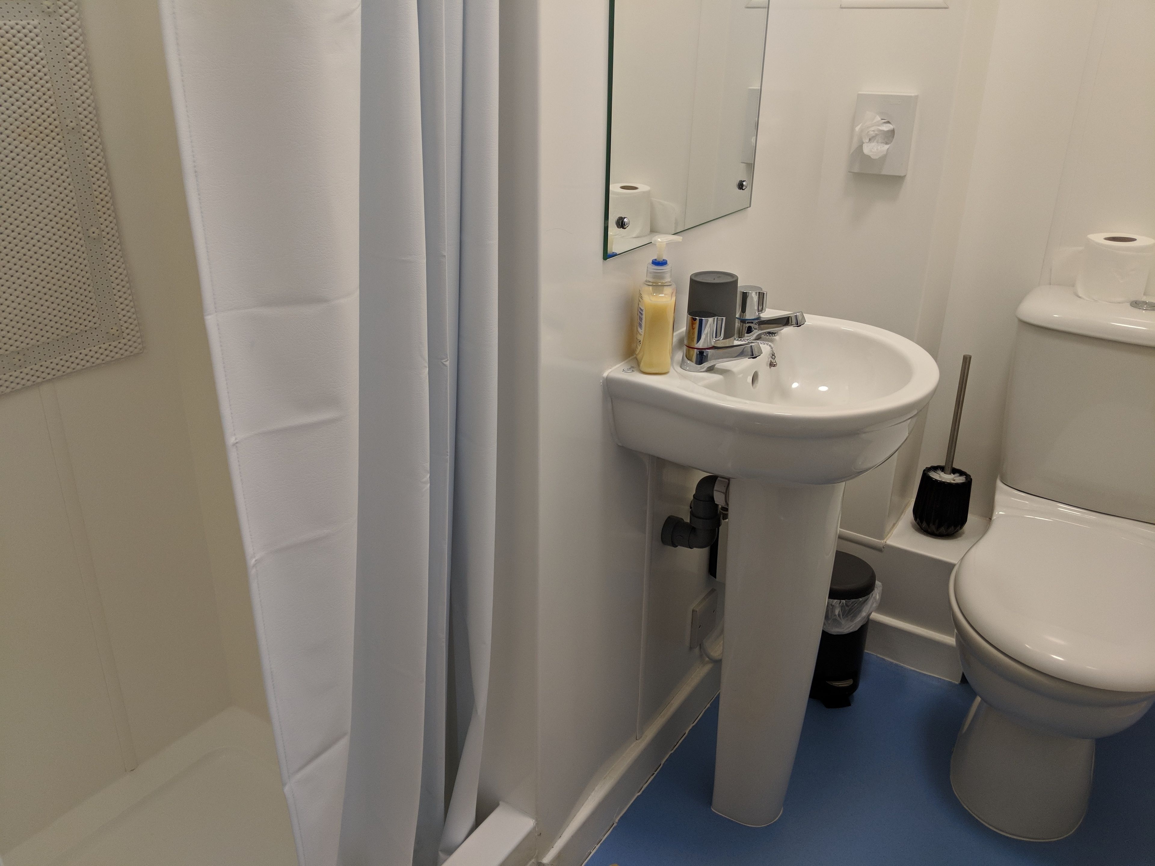 A bathroom with a white sink, mirror, toilet, and blue floor.