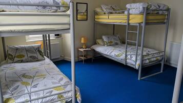 A bunk bed room with a blue carpet, a small table with a lamp, and a window with blinds.