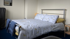 Een slaapkamer met een bed, nachtkastje, lamp en stoel.
