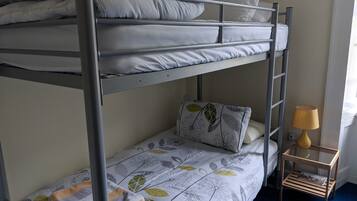 A bunk bed with a patterned bedspread and pillows, a small wooden nightstand with a lamp, and a blue carpet.