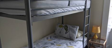 A bunk bed with a patterned bedspread and pillows, a small wooden nightstand with a lamp, and a blue carpet.