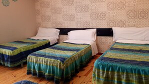 Une chambre avec quatre lits simples, chacun recouvert d’une courtepointe colorée. La chambre est dotée d’un papier peint à motifs et d’un plancher en bois.