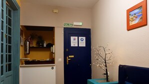 Un hall d’hôtel avec un comptoir d’accueil, une porte bleue portant l’inscription « SORTIE », une petite plante et un tableau encadré accroché au mur.