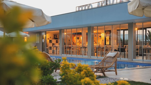 A modern building with a pool, outdoor seating, and a dining area visible through large windows. - La Vida Otel (Urla)