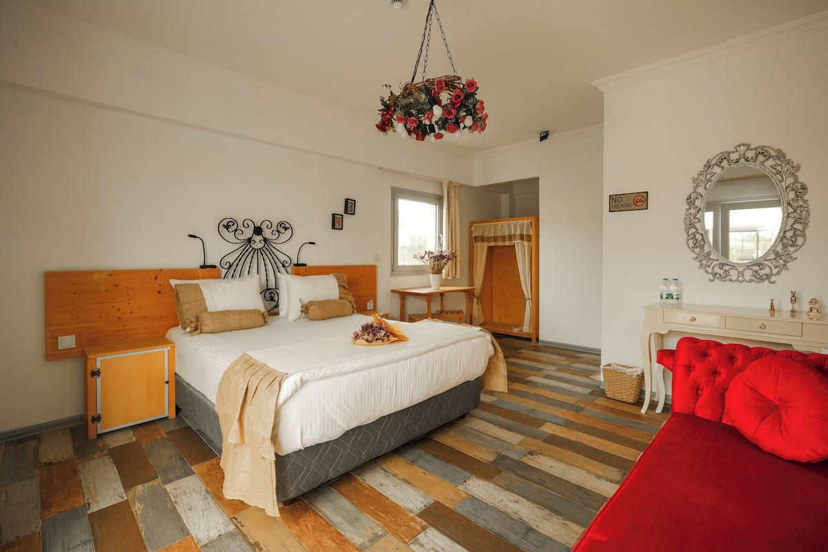 Ein Schlafzimmer mit einem Holzkopfteil, einem Bett mit weißer Bettwäsche, einem roten Sofa, einer floralen Hängeleuchter und einem Spiegel an der Wand.