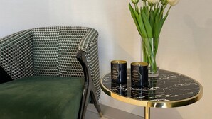 Une pièce comprenant un fauteuil recouvert d’un tissu vert, une table ronde avec un plateau en marbre noir et un vase contenant des tulipes blanches.