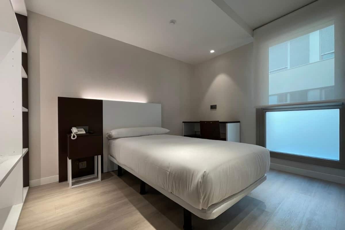 Un dormitorio moderno con cama, mesitas de noche, teléfono y ventana con persianas.