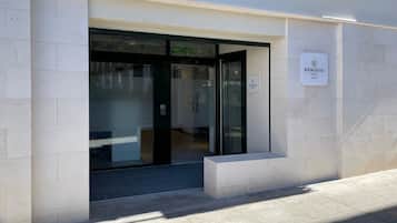 Una entrada de hotel moderna con puerta de vidrio, un cartel y un pequeño espacio al aire libre con mesas y sillas.