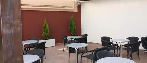 An outdoor patio area with round tables and wicker chairs, a red wall, and two potted plants.