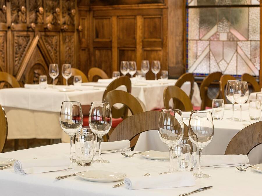 Un comedor con mesas dispuestas para una comida, con manteles blancos y sillas de madera.