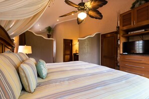 Een hotelkamer met een bed, een plafondventilator, een televisie, houten kasten en een lamp.