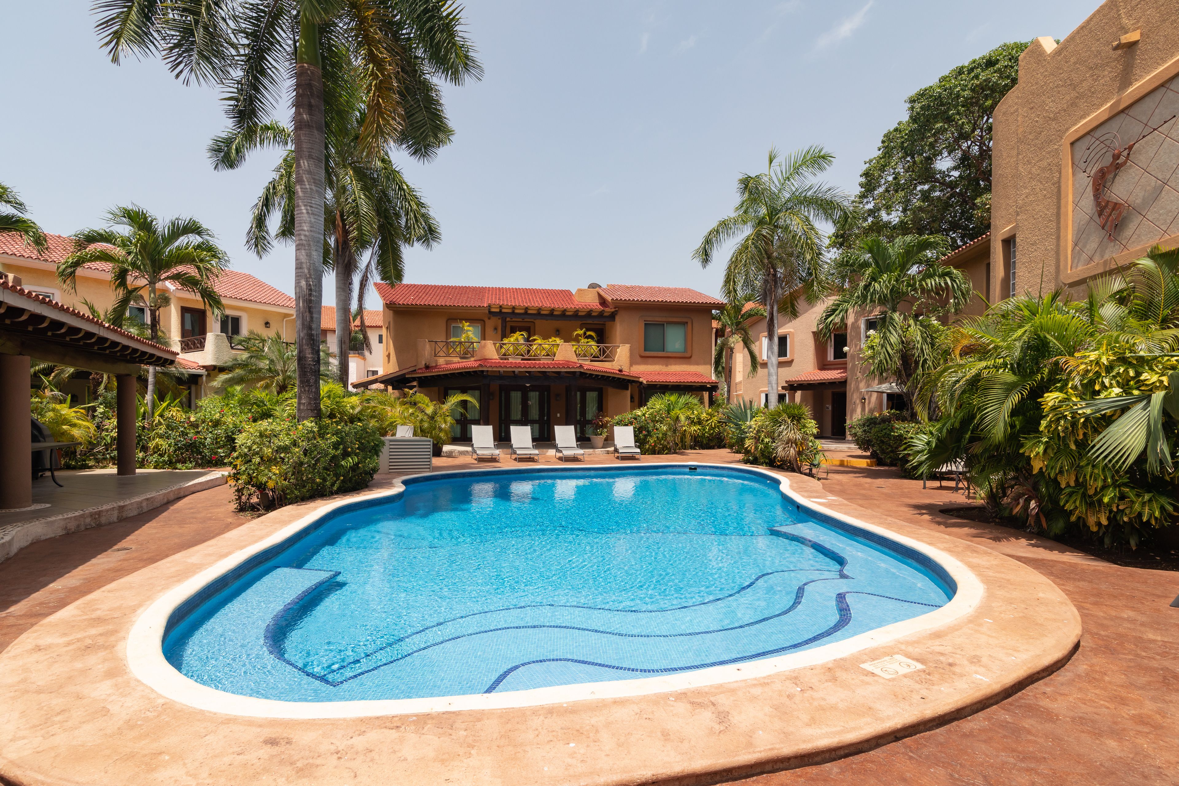 A swimming pool surrounded by palm trees and a building with a red-tiled roof.