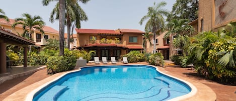 A swimming pool surrounded by palm trees and a building with a red-tiled roof.