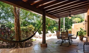 A covered outdoor patio with a hammock, lounge chairs, and a table. - PlayaCar Golf Home by Playa Paradise (Playa del Carmen)
