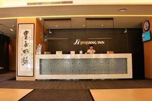 A reception desk with a sign reading 'JINJIANG INN' and a person standing behind it.