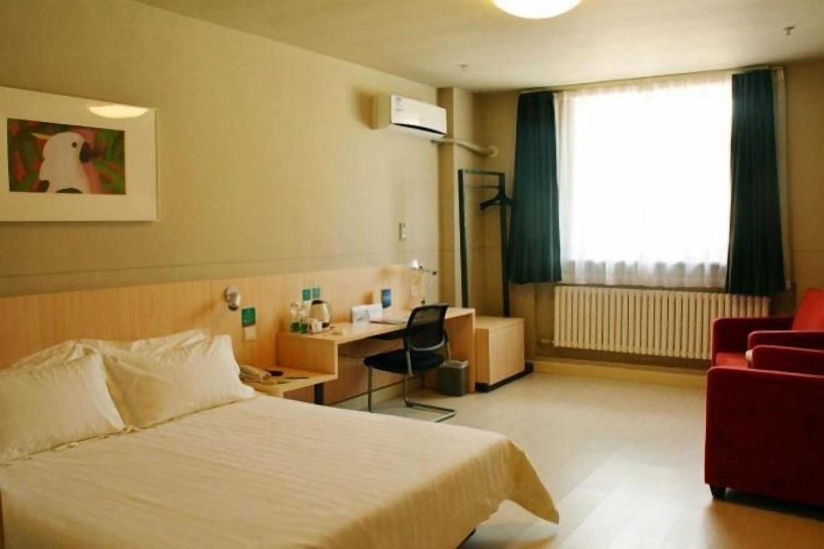 A hotel room with a bed, desk, chair, and a red armchair.