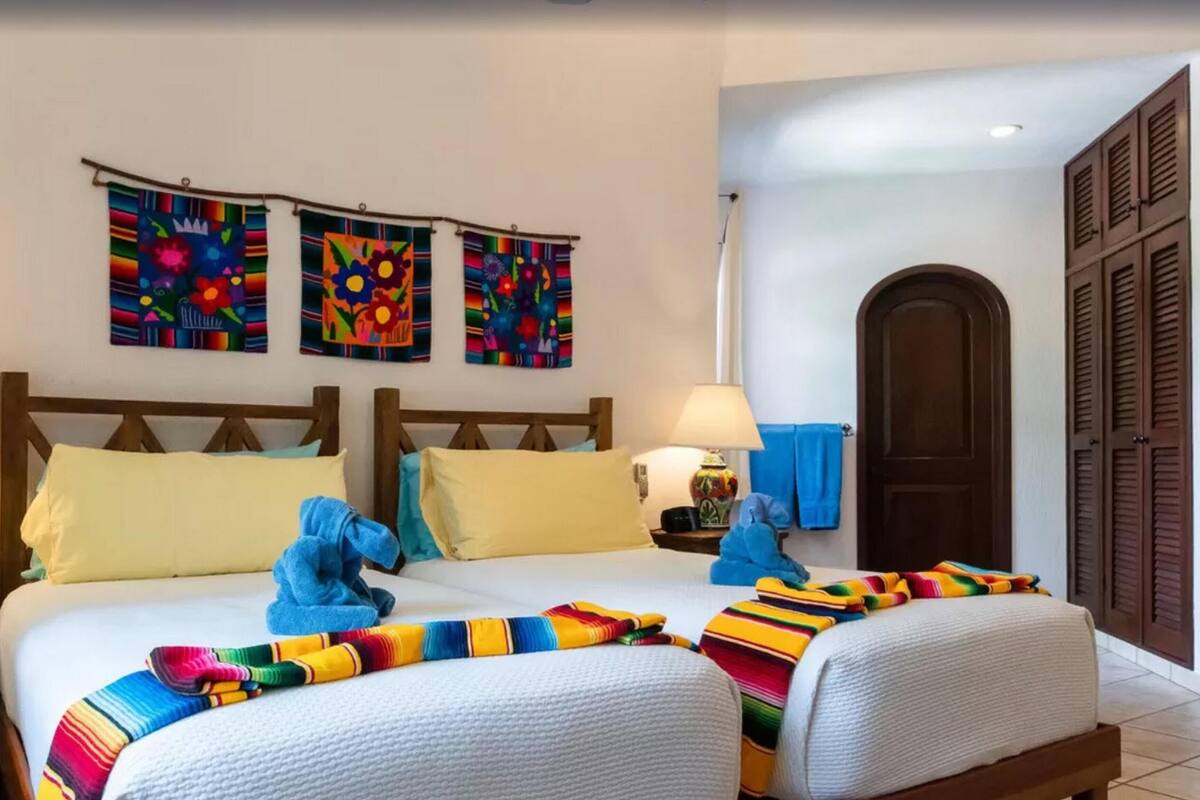 Ein Doppelbett mit bunten Decken und Kissen, ein Holz-Kopfteil und eine Wand mit drei farbenfrohen Kunstwerken.