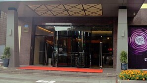 Entrada de hotel con puerta de cristal, alfombra roja y un cartel sobre la puerta.