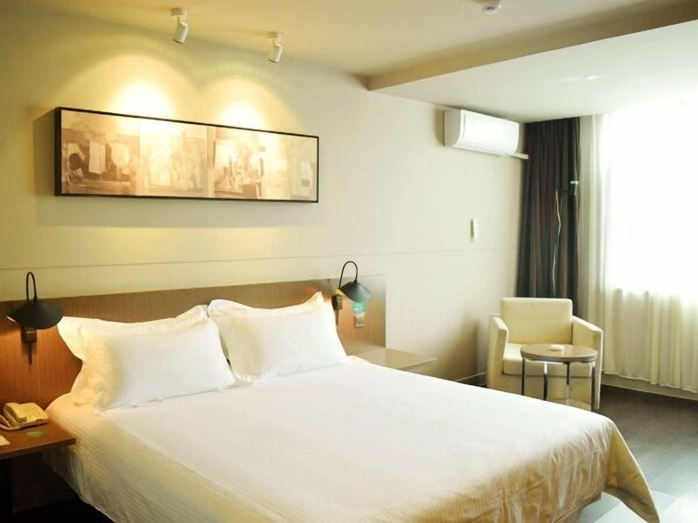 A hotel room with a bed, a chair, a desk with a phone, and an air conditioning unit.