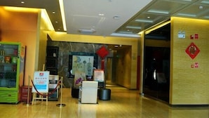 Un hall de hotel con piso de mármol, una máquina expendedora, una mesa de recepción y una pared con detalles decorativos.