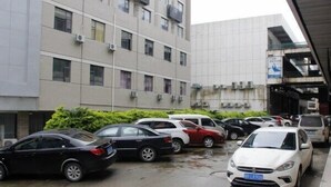 Un estacionamiento con varios autos, un edificio de varios pisos con unidades de aire acondicionado y un corredor cubierto.