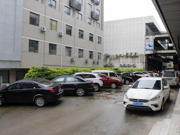 Un estacionamiento con varios autos, un edificio de varios pisos con unidades de aire acondicionado y un corredor cubierto.