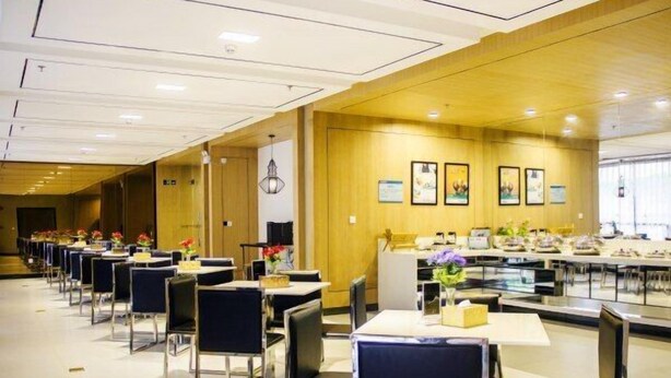 Un comedor de hotel con filas de mesas y sillas, un mostrador de recepción y cuadros en la pared.