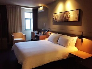 A hotel room with a large bed, a desk, a chair, and a window.