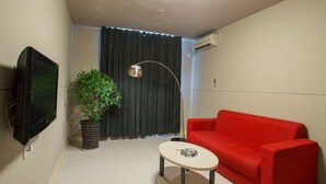 Pieni, moderni olohuone, jossa on punainen sohva, pieni pyöreä pöytä, ruukkukasvi, televisio ja kattovalaisin.